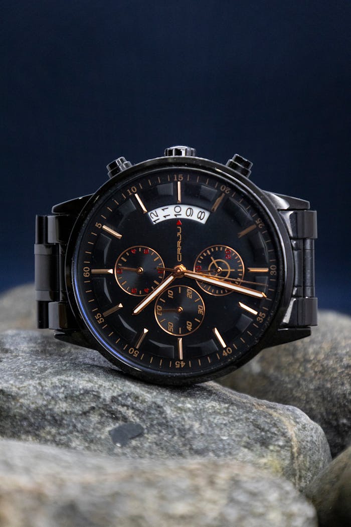 Luxury black and gold analog watch with intricate dials, resting on gray rocks for a sophisticated display.