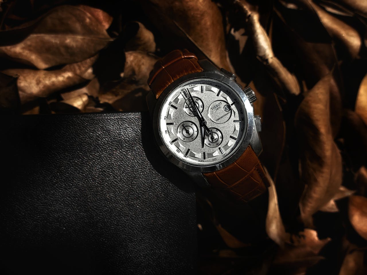 Stylish brown leather wristwatch resting on rustic autumn leaves, showcasing luxury and timeless elegance.
